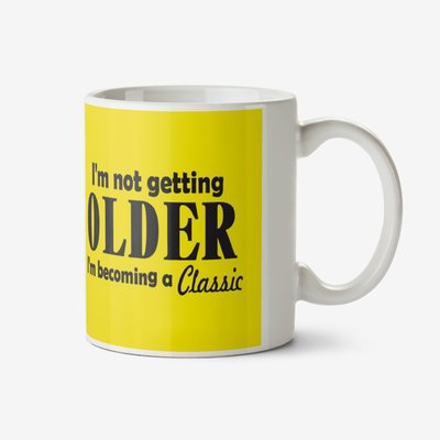 Yellow typographic mug with a caption that reads I'm Not Getting Older, I'm Becoming A Classic